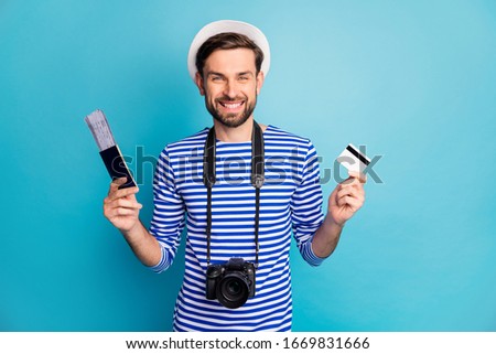 Photo of attractive guy photographer hold professional digital camera traveler buy tickets with help of credit card wear striped sailor shirt vest cap isolated blue color background
