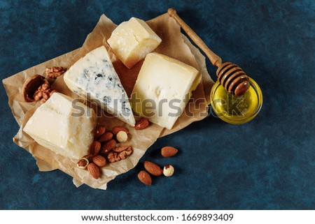 Various sorts of cheese with nuts an honey on a parchment paper on dark blue textured background. Top view