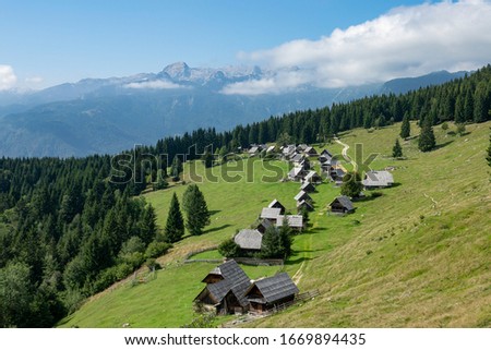 AERIAL: Flying over a row of traditional mountain cottages in scenic Pokljuka, Slovenia. Breathtaking view of a remote village in the Julian Alps on a sunny summer day. Traditional Slovene huts. Royalty-Free Stock Photo #1669894435