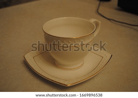 Empty Porcelain saucer and a cup with pattern and yellow bordure. Cup of tea-coffee on the table with a tablecloth. White and simple tea set. 