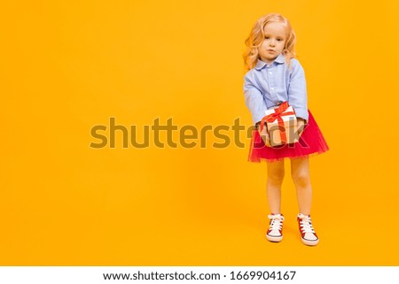 Beautiful girl with long hair smiles and holds a gift, picture isolated on yellow background