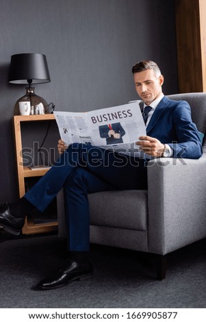 businessman in suit reading newspaper with business lettering and sitting in armchair