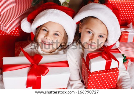 Portrait of Santa hat Christmas girls holding christmas gifts smiling happy and excited. Cute beautiful santa children on red background.