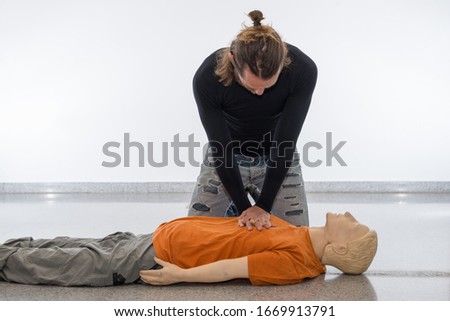 Man teaching cardiopulmonary resuscitation with a dummy on a white background. Performing chest compressions for cardiac massage (Photo 13 of 18).
