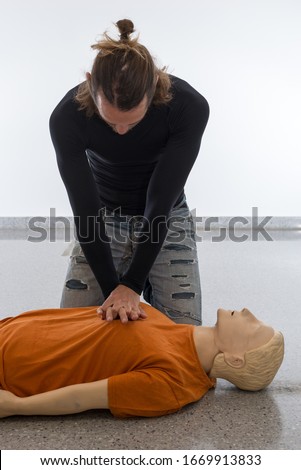 Man teaching cardiopulmonary resuscitation with a dummy on a white background. Placing one hand over another hand for cardiac massage (Photo 15 of 18).
