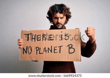 Young handsome man with beard asking for environment holding banner with earth message annoyed and frustrated shouting with anger, crazy and yelling with raised hand, anger concept