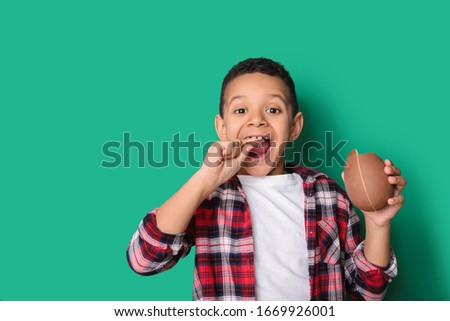 Cute African-American boy with sweet chocolate egg on color background Royalty-Free Stock Photo #1669926001