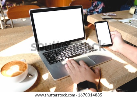 Close up of woman using cell phone and laptop,sending massages within the cafe.having sunbath.Phone with black screen,texting,video calls.