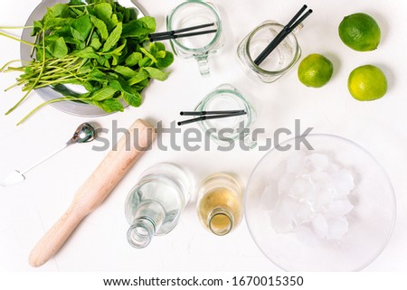 Ingredients for making mojito. Alcoholic refreshing summer drink. Mint, glass goblets, rum, syrup and lime on a white background.