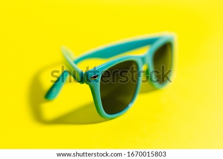 Close-up of cyan sunglasses, on background of yellow color.
