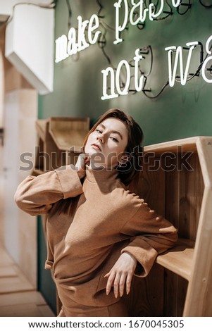 Make pasta, not war. Stylish girl stands near a wooden shelf in a modern interior. Neon sign.