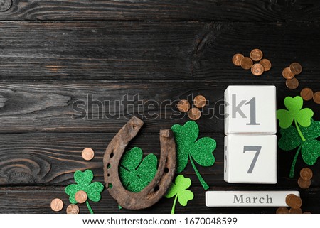 Flat lay composition with horseshoe and block calendar on black wooden background, space for text. St. Patrick's Day celebration