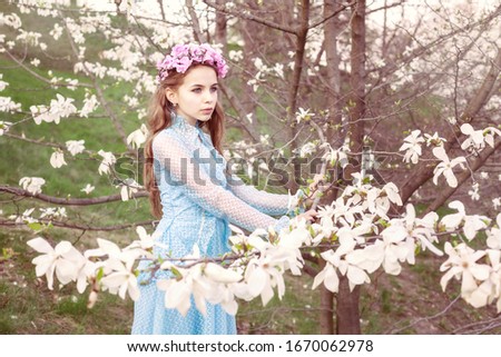 Beautiful young girl standing near a magnolia tree and looks into the distance.