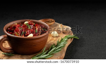 Sun-dried tomatoes with garlic, rosemary and spices in a clay bowl on an olive wood cutting board, copyspace