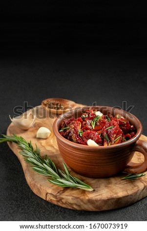 Sun-dried tomatoes with garlic, rosemary and spices in a clay bowl on an olive wood cutting board, vertical image with copyspace
