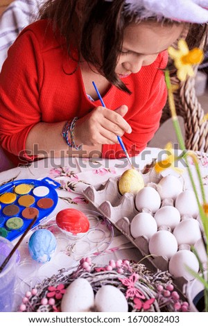 little girl in the ears of a rabbit coloring easter eggs. Fun activities on Easter Sunday, decor and flowers. Copy space. Vertical photo
