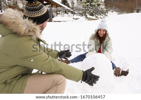 Happy couple making ball for snowman outdoors. Winter vacation