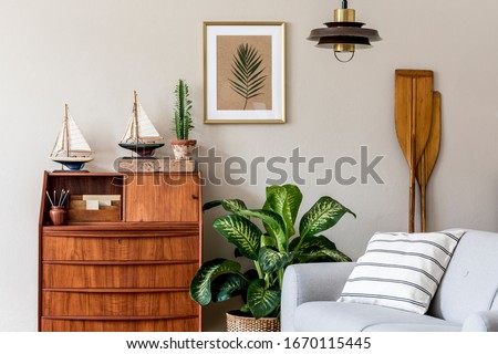 Stylish and vintage interior design of open space with wooden retro cabinet, design sofa, pendant lamp, ships, cacti, plants and elegant personal accessories in modern vintage home decor.