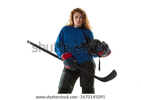 Young female hockey player with the stick on ice court and white background. Sportswoman wearing equipment and helmet posing. Concept of sport, healthy lifestyle, motion, action, human emotions.