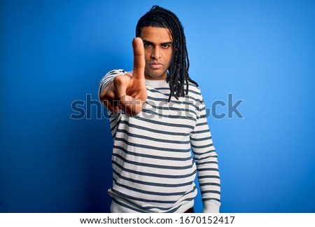 Young handsome african american afro man with dreadlocks wearing casual striped sweater Pointing with finger up and angry expression, showing no gesture