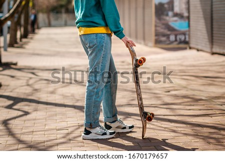 A young teen poses with a skateboard. In the background, an alley. Close up. Concept of sports lifestyle and street culture