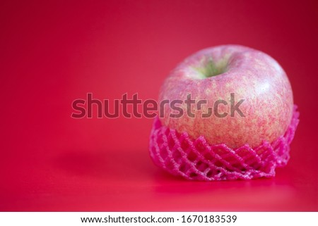 Fresh of apple wrapped with foam fruit net on red background.