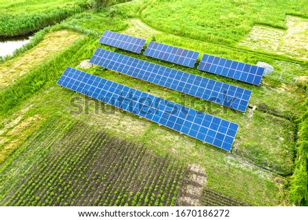 Blue solar photo voltaic panels mounted on metal frame standing on ground with green grass in field.