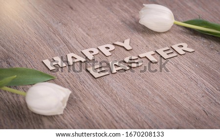 Wooden letters on wooden background with text "Happy Easter" and white tulips decoration