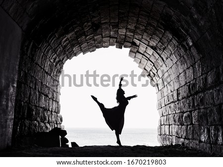 Dancer, graceful woman dancing in the arch, ballet dancer. ballerina dancing in the old fortification place. Contrast, silhouette of girl figure on sunny day. Woman figure. Black and white photo
