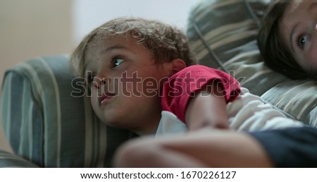Two brother and sister children watching movie at night lying on sofa