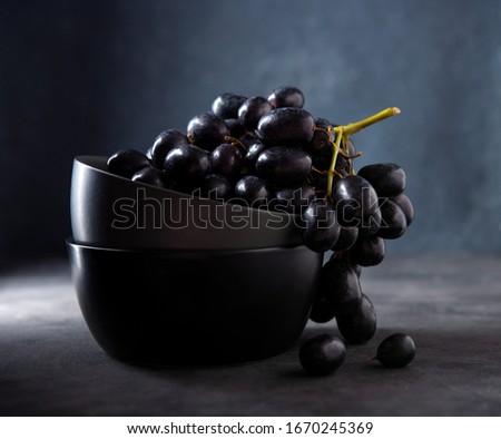 a cluster of juicy black grapes lies in a dark gray bowl on a dark gray table. Photo dark and mood. Front and macro view