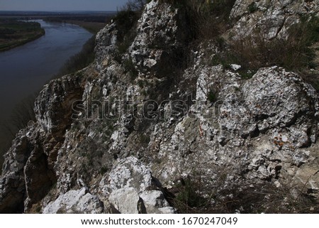 Gray granite rock near the river on a Sunny spring day against the blue sky, a cliff from a height, a top view of the shore and the flow of water