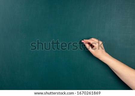 Hand with chalk on a green blackboard background. Handwriting concept on blackboard.