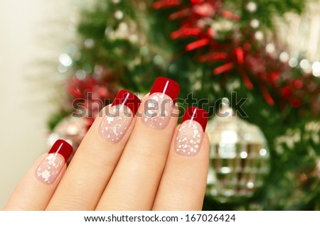 Winter manicure with red lacquer and white chips on the background of the Christmas tree. Royalty-Free Stock Photo #167026424