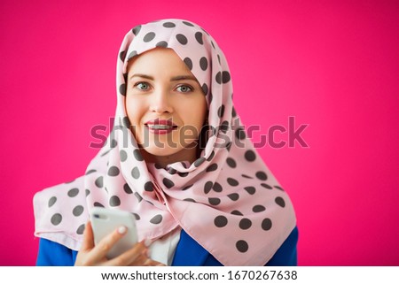 beautiful young woman in a scarf on a pink background with a phone in her hand