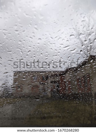 raindrops on glass against a gray sky and a blurry brick building