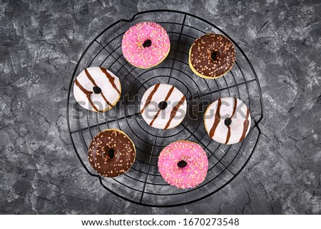 Glazed donuts with different white and brown chocolate and strawberry topping with sprinkles arranged in circle on cake grid on dark grunge background