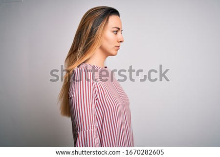 Young beautiful blonde woman with blue eyes wearing stiped t-shirt over white background looking to side, relax profile pose with natural face with confident smile.