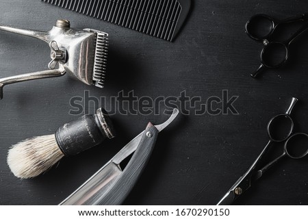 On a black dusty surface are old barber tools. Vintage manual hair clipper comb razor shaving brush shaving brush hairdressing scissors. black monochrome.
