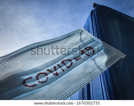 COVID 19 Coronavirus on Medical Protective Mask. Blue Suitcase Concept for Travelling in Corona Virus Outbreak Season. Travel ban block forbidden. Pandemy of Korona Virus Spreading all over the World Royalty-Free Stock Photo #1670302735