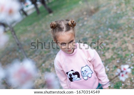 Portrait of a beautiful happy little girl on a background of blooming pink almonds, outdoor