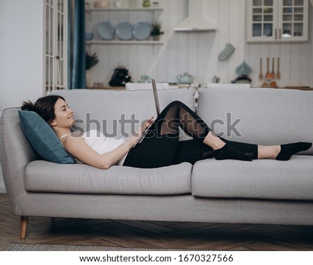Portrait of casual woman working at home with laptop while sitting at sofa in living room.