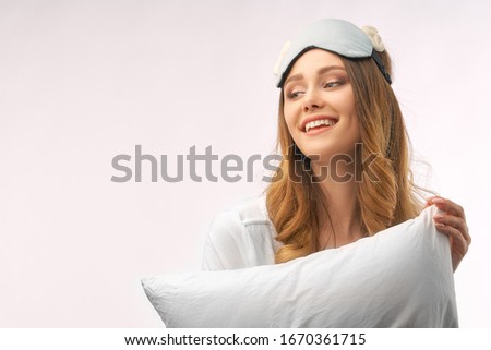 Photo shot of glad happy woman holds soft white pillow, sleeps well at night, enjoys rest, comfort and leisure, has cheerful expression. Beautiful lady model is standing at white background in Studio.