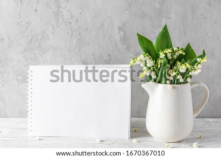 Blank greeting card with spring lily of the valley flowers in vase on concrete background with copy space. mock up. still life. holiday or wedding background