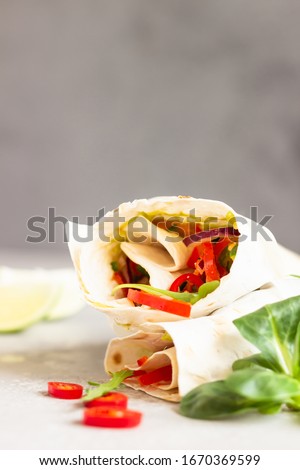 Wrap sandwiches with vegetable salad, chili pepper and lime on a light grey stone background. 