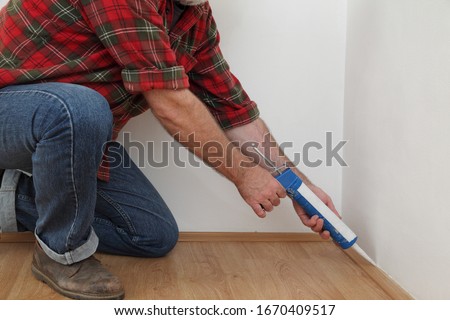 Construction worker caulking  batten of laminate floor using silicone glue in a cartridge, closeup of hands, home renovation Royalty-Free Stock Photo #1670409517