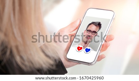 young woman operates smartphone display with online dating app deciding dislike or like button, while watching mature handsome man portrait. light city environment with blurry background bokeh effect