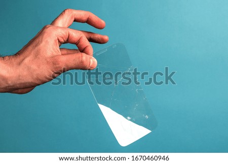 man holds broken, broken smartphone safety glass in his hand on blue background. concept of fragile equipment