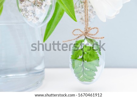 Easter minimal composition, white tulips, transparent glass egg filled with white flowers and fern leaves on grey background. Eco Stylish decor concept. Copy space. Festive greeting card, front view
