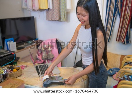 Young woman showing/holding pos payment terminal or credit/debit cards swiping machine In a clothing store
